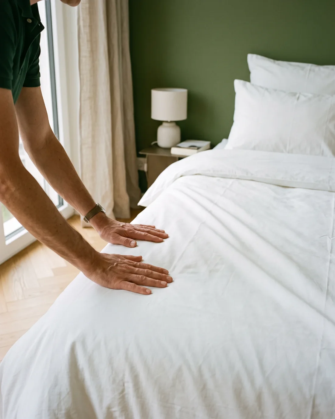 Mains lissant une couette blanche sur un lit préparé entre deux séjours